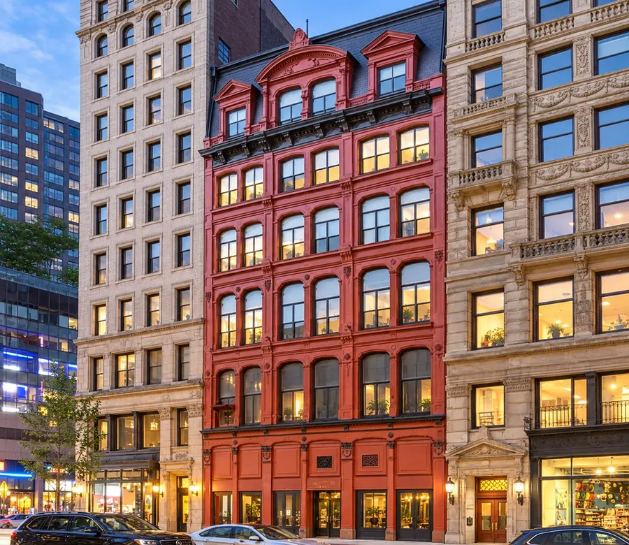 836-838 Broadway, a red cast-iron building with arched windows and a mansard roof, at dusk